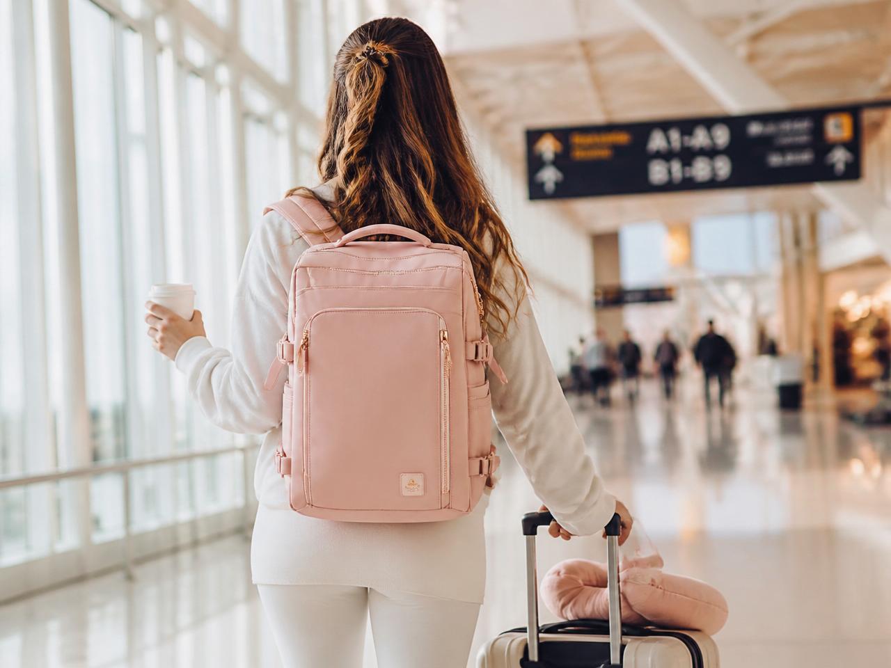 Woman walking through an airport with the pink LunaPack travel backpack